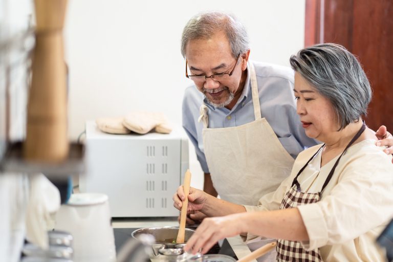Asian Senior elderly couple cooking food with smiling face in kitchen. Loving older grandparents feeling happy and enjoy retirement life together in house. Relationship Healthcare and activity at home